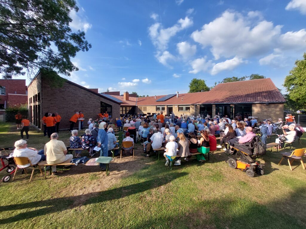 Sommerkonzert von SinnersBlow 2025 im Garten der Ev. Gemeinde, Publikum von hinten (c) Dieter Urban